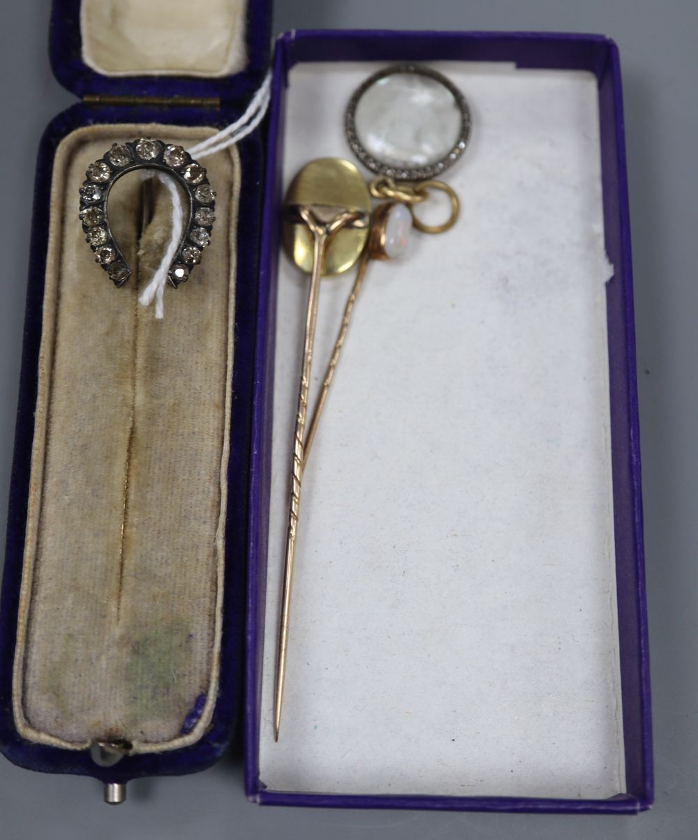 A diamond horseshoe stick pin, two other stick pins and a pendant